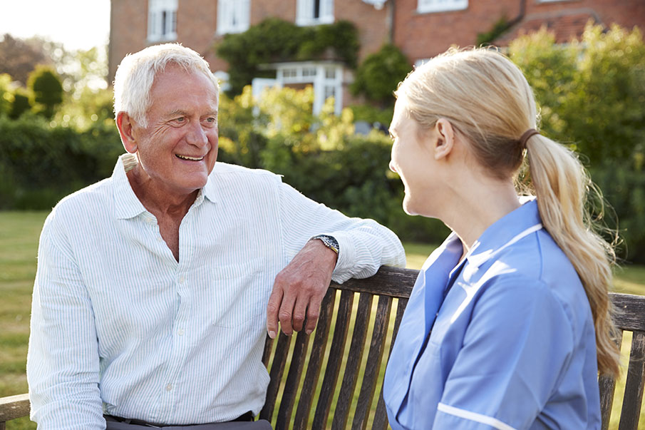 Care home resident with a nurse, sitting on a bench in the care home grounds